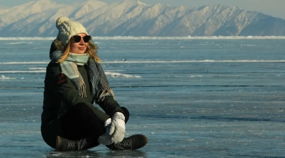 Woman sitting on the frozen ice of Lake Baikal during a winter tour on Olkhon Island