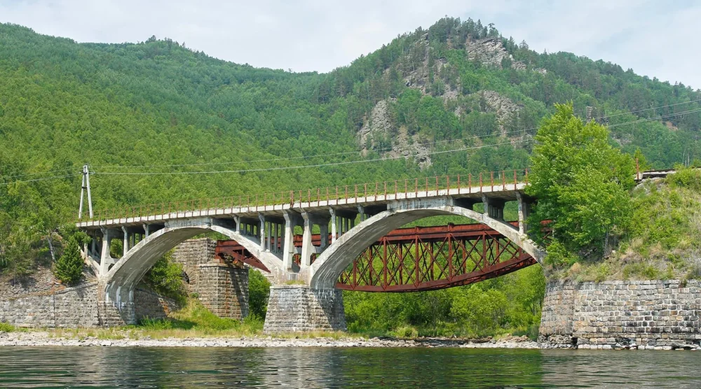 Historic stone arch bridge of the Circum-Baikal Railway over water with forested mountains in the background
