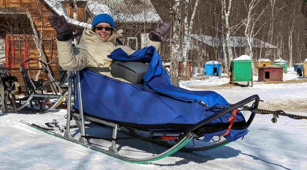 A happy woman sitting in a blue dog sled during a husky sledding tour at Lake Baikal
