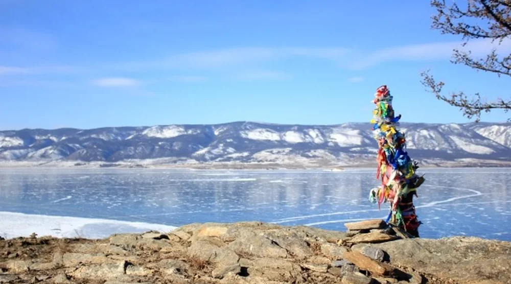 Traditional shamanic ritual ribbons on a wooden pole overlooking frozen Lake Baikal and snow-capped mountains on Olkhon Island