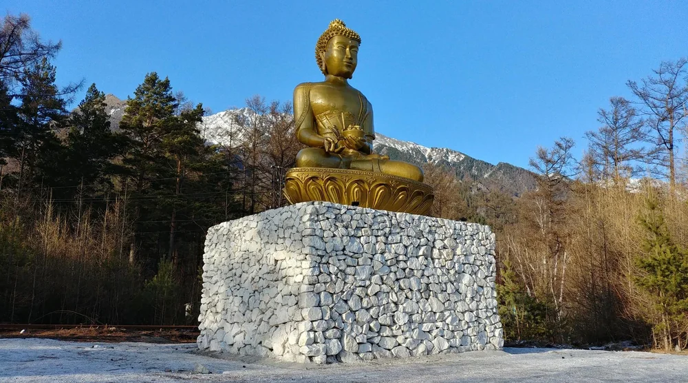 Golden Buddha statue on a stone pedestal with mountains in the background in Arshan, Buryatia