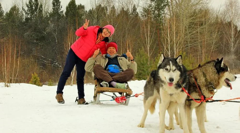 Happy tourists posing with huskies and a sled during a dog sledding tour at Lake Baikal
