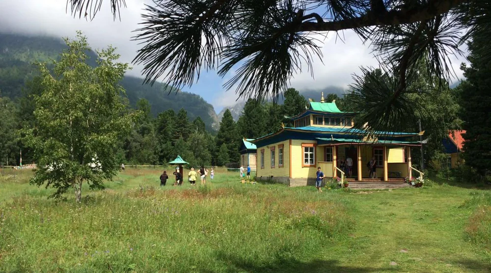Traditional yellow building with a blue roof in Arshan village surrounded by green mountains and trees