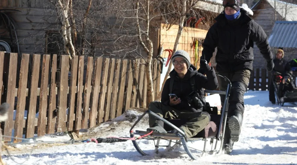 A smiling woman enjoying a husky dog sledding tour on the snow near Lake Baikal