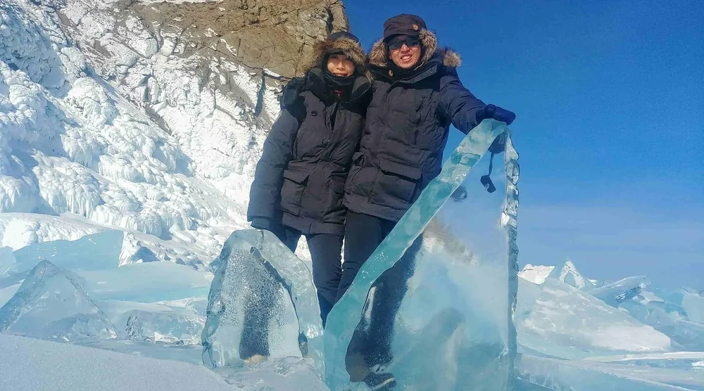 Two women smiling and posing behind large ice chunks on Lake Baikal during a winter tour in Listvyanka