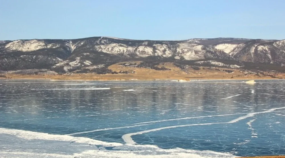Frozen Lake Baikal with ice cracks and snow-capped mountains in the background during winter tour