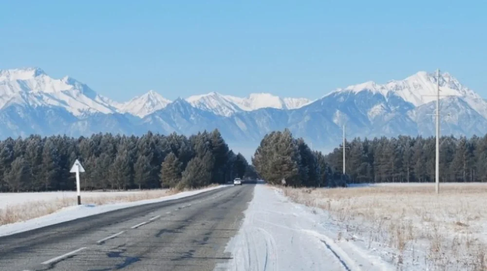 Scenic road through snow-covered Tunka Valley with majestic mountains in the background during Arshan tour
