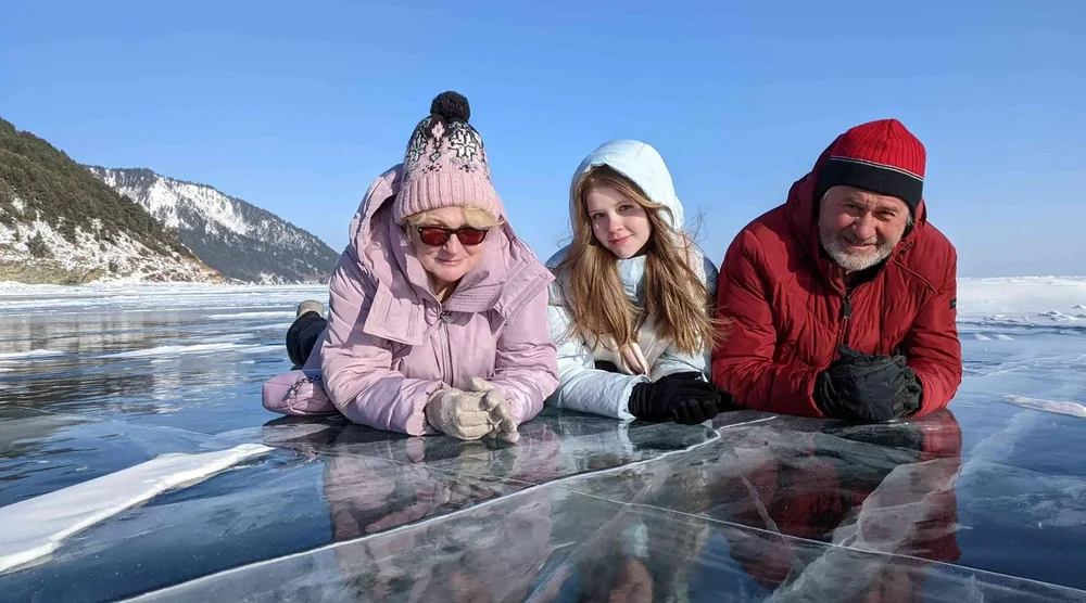 A family lying on the clear frozen ice of Lake Baikal during a winter tour in Listvyanka