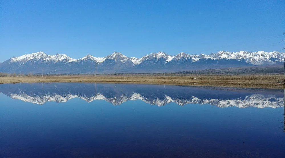 Snow-capped mountains of Arshan reflected in a calm lake in Buryatia