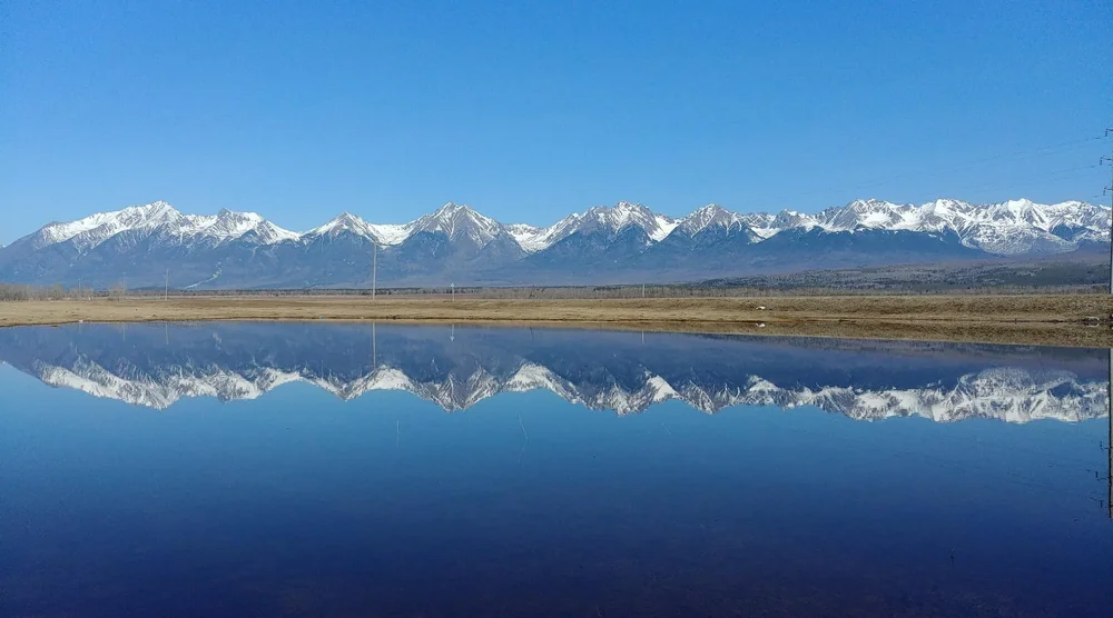Snow-capped mountains of Arshan reflected in a calm lake in Buryatia