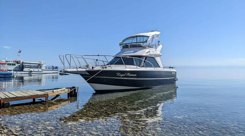 A motorboat named Royal Platinum docked near a wooden pier on the clear waters of Lake Baikal during a summer tour in Listvyanka