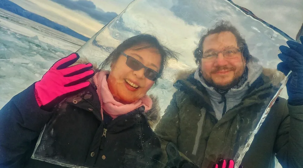 Smiling tourists holding a large piece of clear blue ice from Lake Baikal during an Olkhon Island winter tour