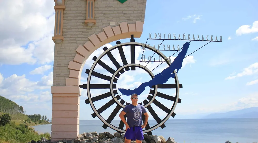 Tourist posing in front of the Circum-Baikal Railway monument with Lake Baikal in the background